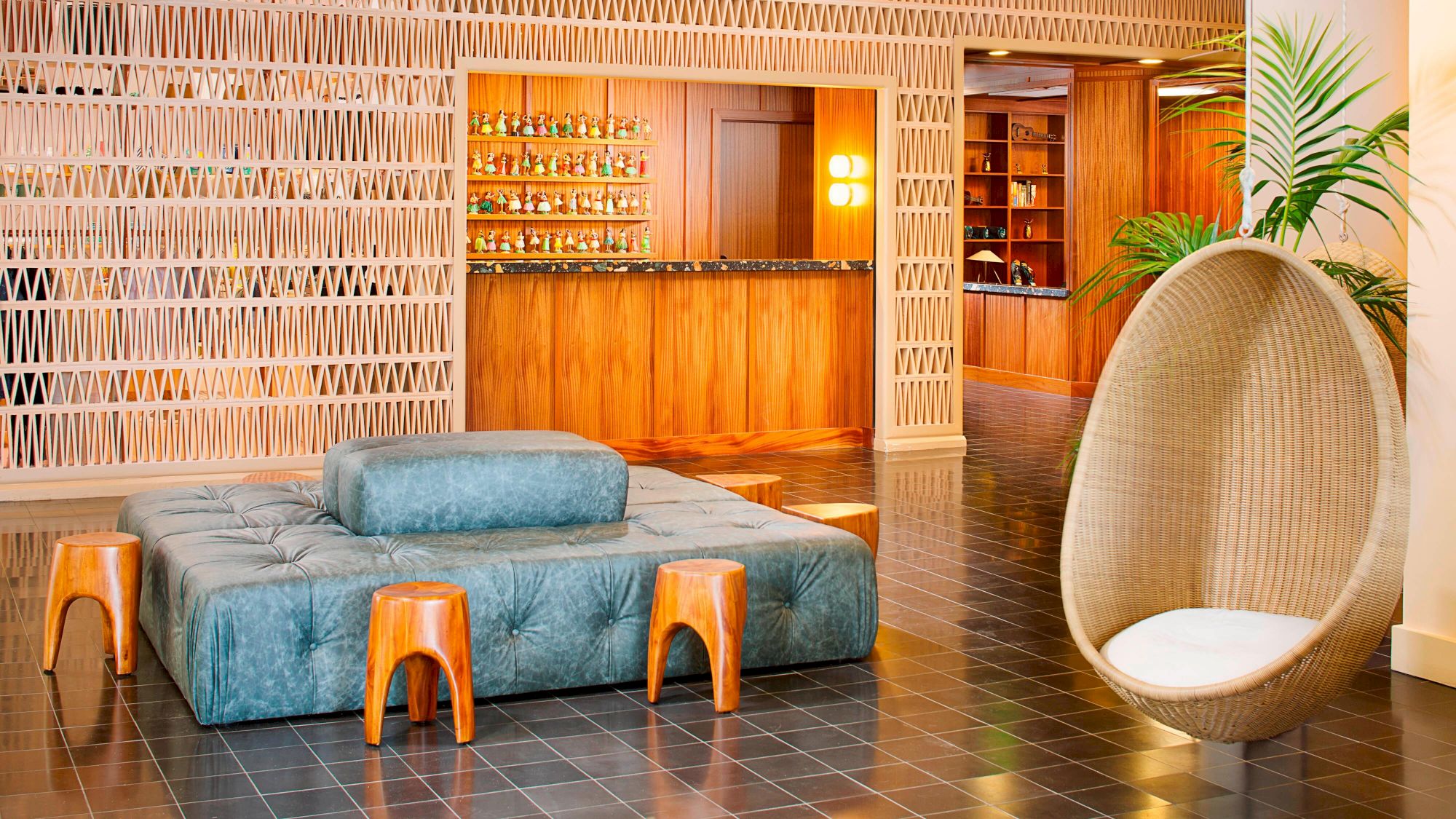 A modern lounge area with a blue cushioned bench, wooden stools, an egg-shaped chair, and a wooden bar in the background.