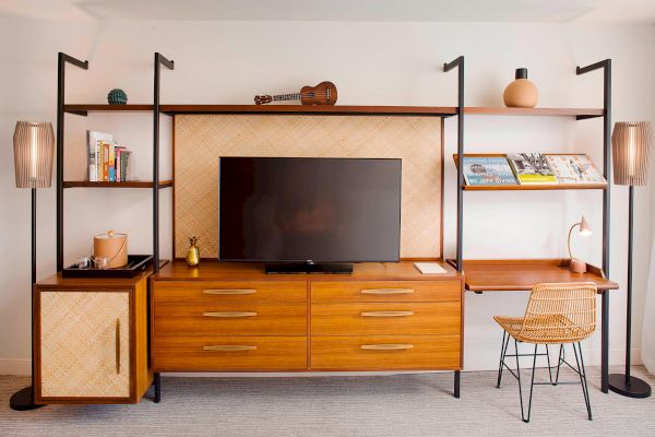 A stylish wooden entertainment unit with a TV, books, magazines, a small guitar, decorative items, and a desk with a chair.