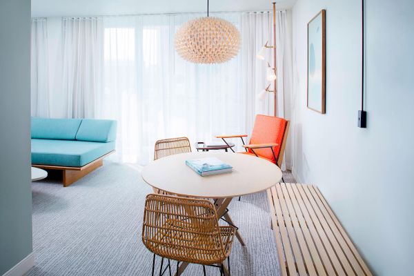 A modern living room with a blue sofa, round table, wicker chairs, and unique lighting. Light colors and natural textures create a cozy space.