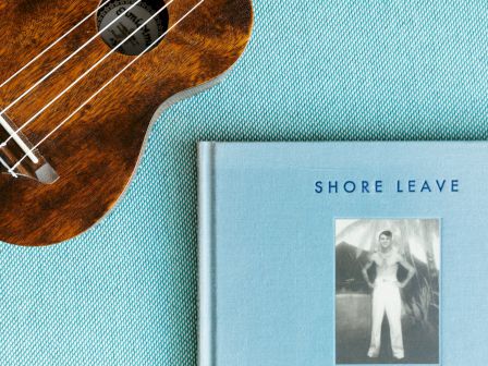A ukulele and a book titled "Shore Leave" by Ryan Mungia are on a textured surface.