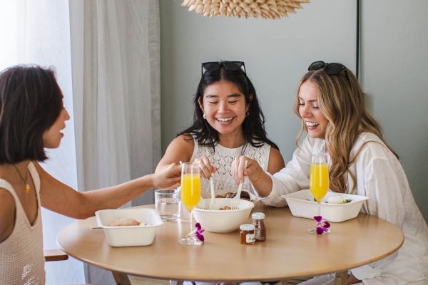 Three people sit at a round table enjoying drinks, surrounded by bright decor, and sharing a cheerful moment together.