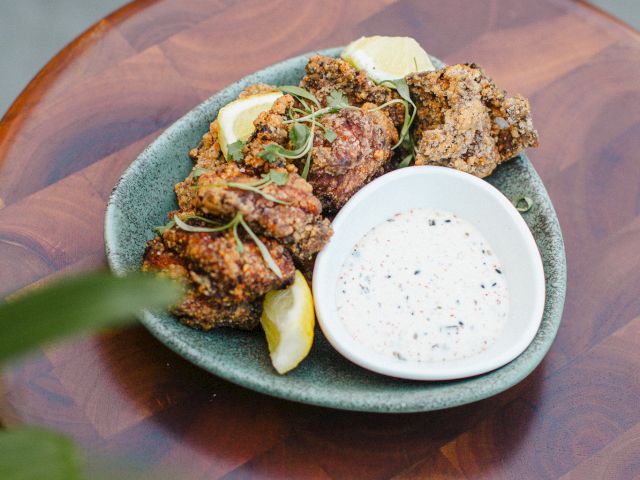 A plate of fried chicken pieces with lemon wedges and a bowl of dipping sauce on a wooden table.