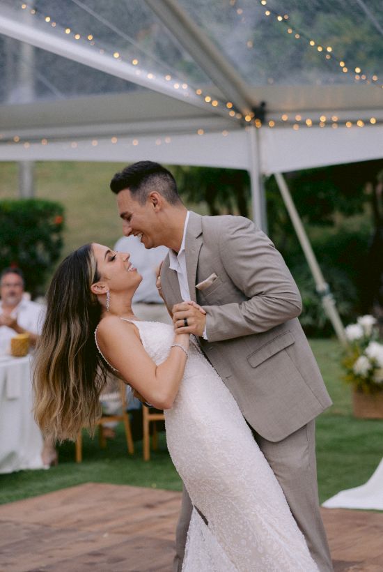 A couple is dancing closely in a wedding setting under a canopy, surrounded by soft lighting and greenery.