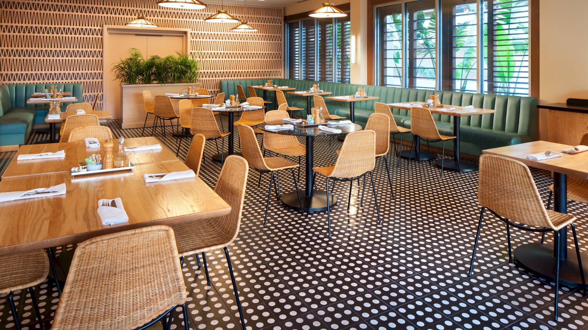 A chic restaurant interior with wooden tables, wicker chairs, patterned flooring, and stylish lighting. Greenery adds a touch of freshness.