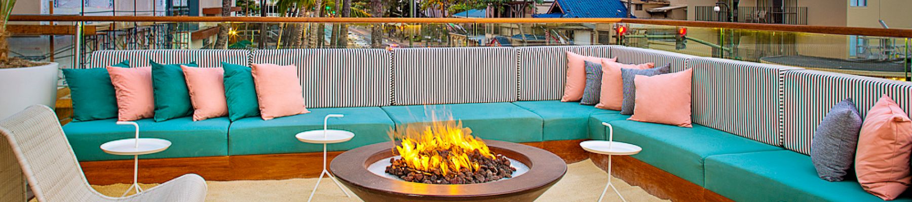 A cozy outdoor seating area with a fire pit, surrounded by vibrant cushions and buildings, offers a relaxing urban retreat.