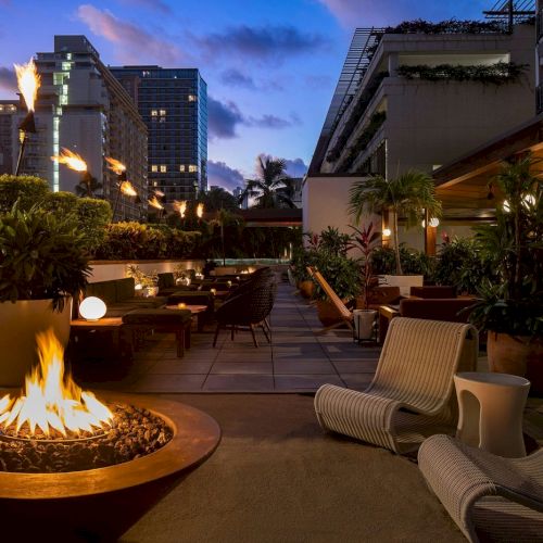 A stylish outdoor lounge with modern seating, a fire pit, and ambient lighting at dusk. Bathed in a warm and inviting atmosphere.