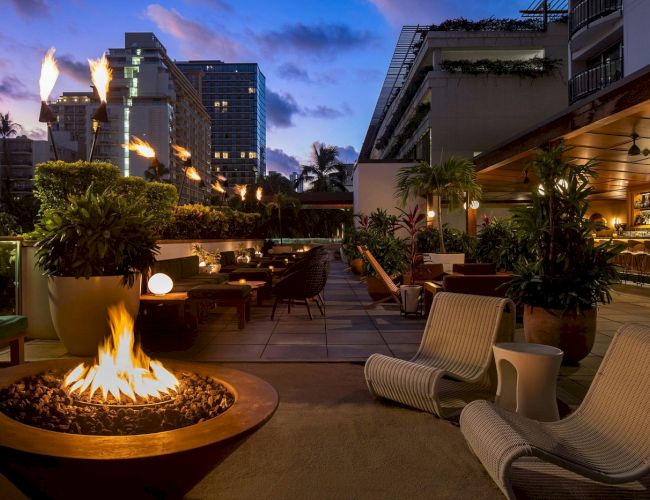 A stylish outdoor lounge with modern seating, a fire pit, and ambient lighting at dusk. Bathed in a warm and inviting atmosphere.