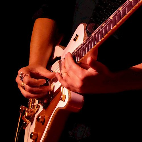 A person playing an electric guitar, focusing on their hands and the instrument in a dimly lit setting.