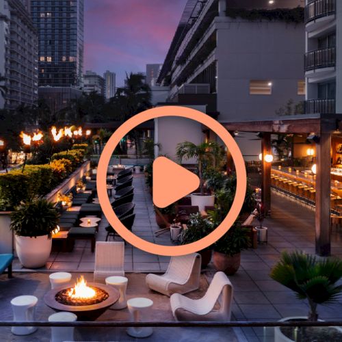 The image depicts an upscale outdoor rooftop lounge at twilight, featuring a fire pit, modern seating, and lush greenery under a colorful sky.