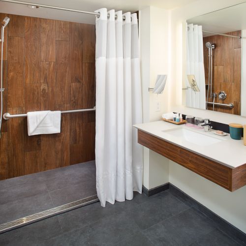 This image shows a modern bathroom with wood and tile accents, featuring a shower with a curtain, and a vanity with a sink and mirror.