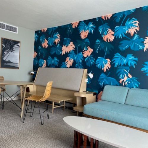 A room with a tropical-themed wall, wooden furniture, a blue couch, and a table, creating a relaxed and modern atmosphere.