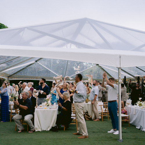 A group of people celebrating under a transparent tent at an outdoor event, with tables and decorations around them.