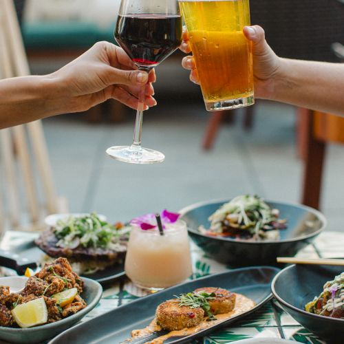 Two people toast with wine and beer over a table filled with various dishes, creating a festive dining atmosphere.